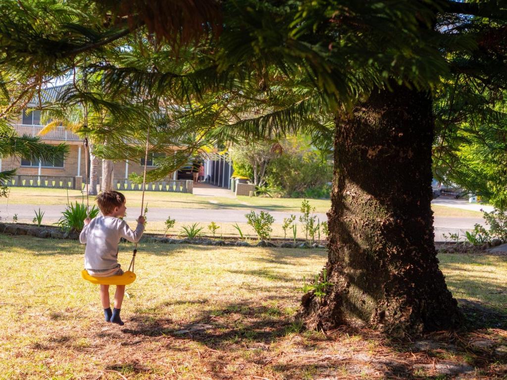a little girl is playing in the grass next to a tree at Collingwood Beach Cottage - Belle Escapes Jervis Bay in Vincentia