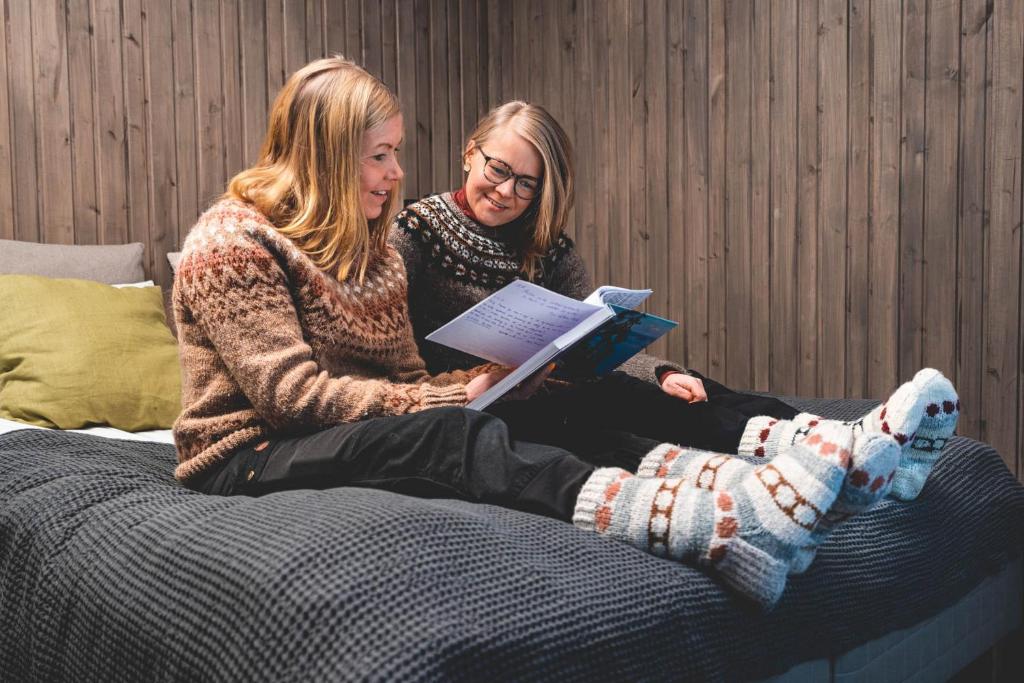 two women sitting on a bed reading a book at Venejoen Piilo - Päre in Kontiolahti