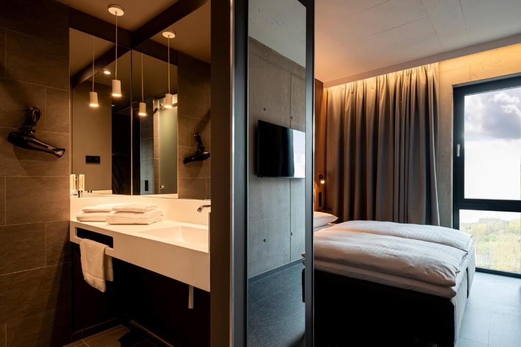 uma casa de banho com um lavatório, uma cama e um espelho. em Zleep Hotel Zürich-Kloten em Kloten