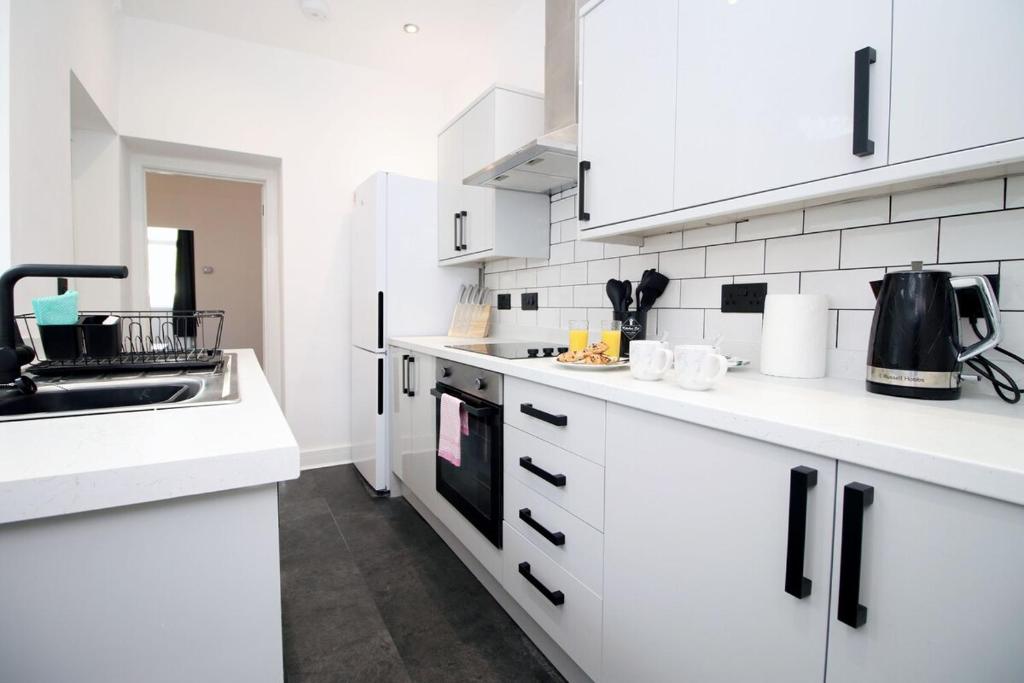 a white kitchen with white cabinets and a sink at 3 Bedroom House in Mountain Ash Cynon View by TŷSA in Quakers Yard