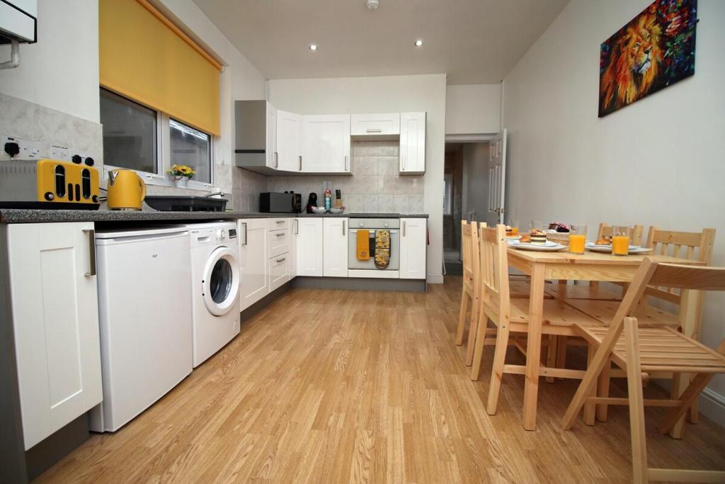 uma cozinha com armários brancos, uma mesa e uma máquina de lavar roupa em Camelot House by Tŷ SA em Newport