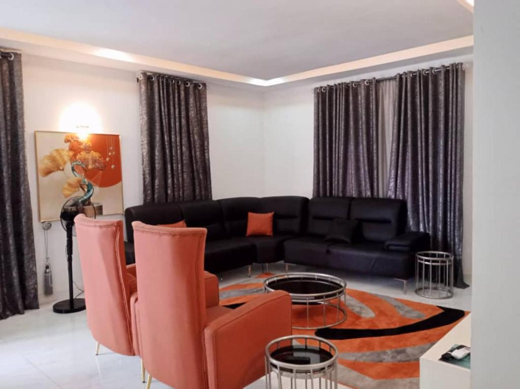 uma sala de estar com um sofá preto e cadeiras laranja em Dixonlux Apartments em Abuja
