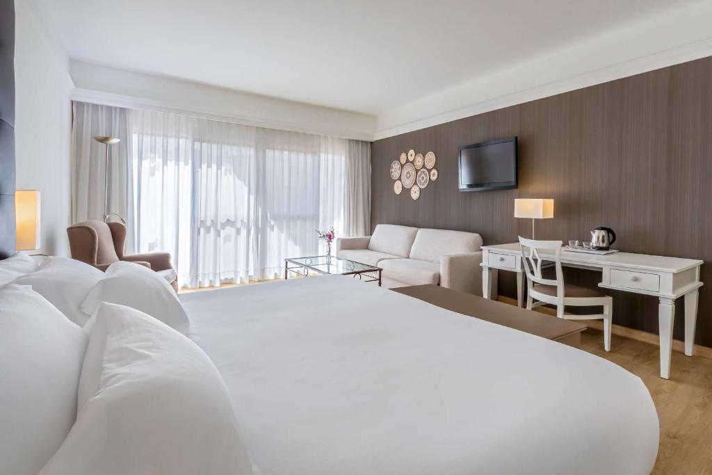 a hotel room with a white bed and a desk at Barceló Corralejo Bay - Adults Only in Corralejo