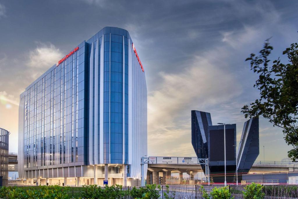 un grand bâtiment en verre avec un panneau rouge sur lui dans l'établissement Hilton Garden Inn London Heathrow Terminal 2 and 3, à Hillingdon