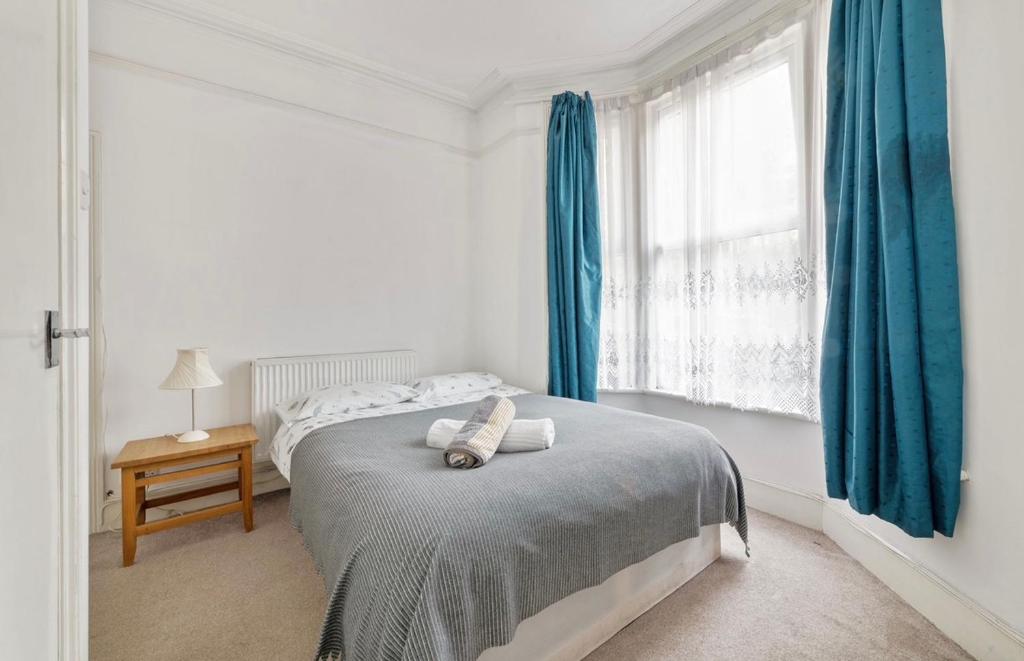 a bedroom with a bed with blue curtains and a window at Calderon Road in London