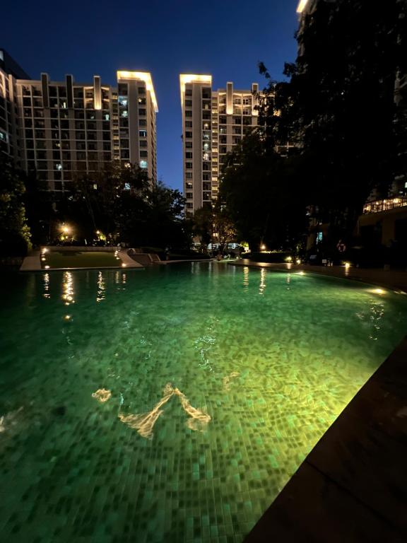 een groot zwembad van groen water met gebouwen op de achtergrond bij Parkland Srinagarindra A in Bangna