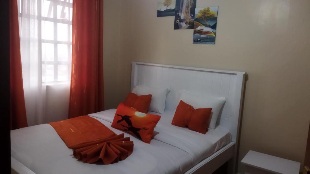 1 dormitorio con cama blanca y almohadas de color naranja en Lacasa accommodation, en Naivasha
