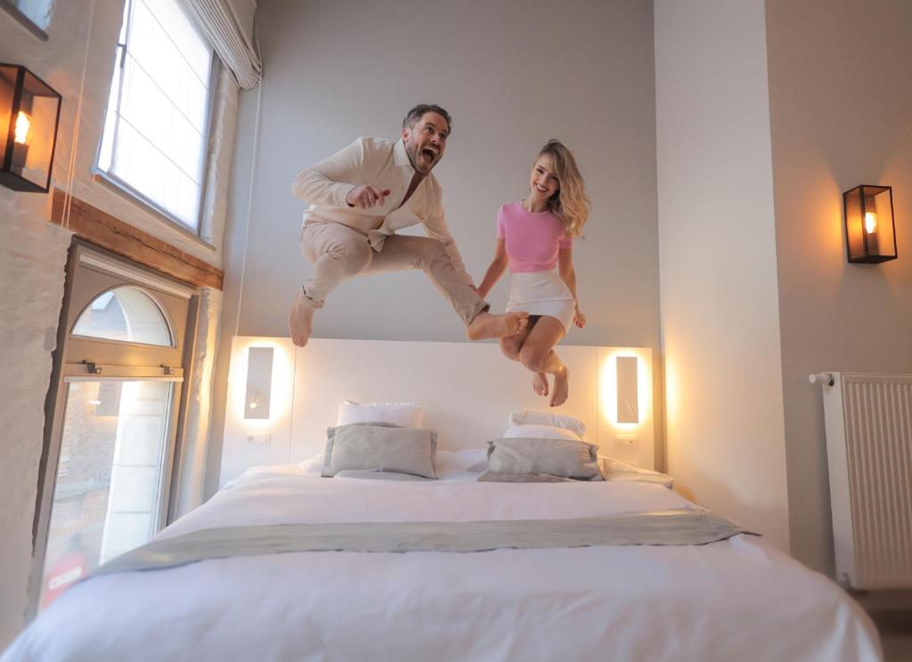 a man and woman jumping on top of a bed at Martin's Brugge in Bruges