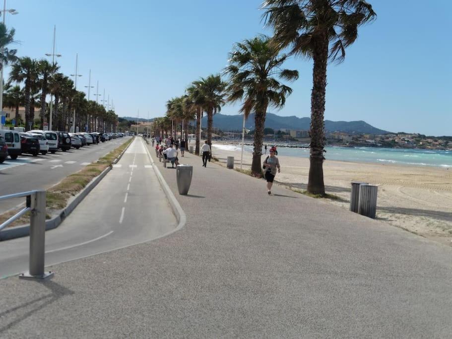 uma rua com palmeiras e pessoas caminhando na praia em T2 avec grand jardin,plage à pieds quartier des Lônes em Six-Fours-les-Plages