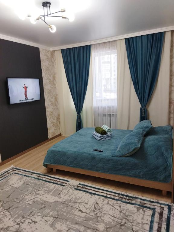 Cette chambre comprend un lit avec des draps bleus et une télévision. dans l'établissement Квартира в новом районе, à Öskemen