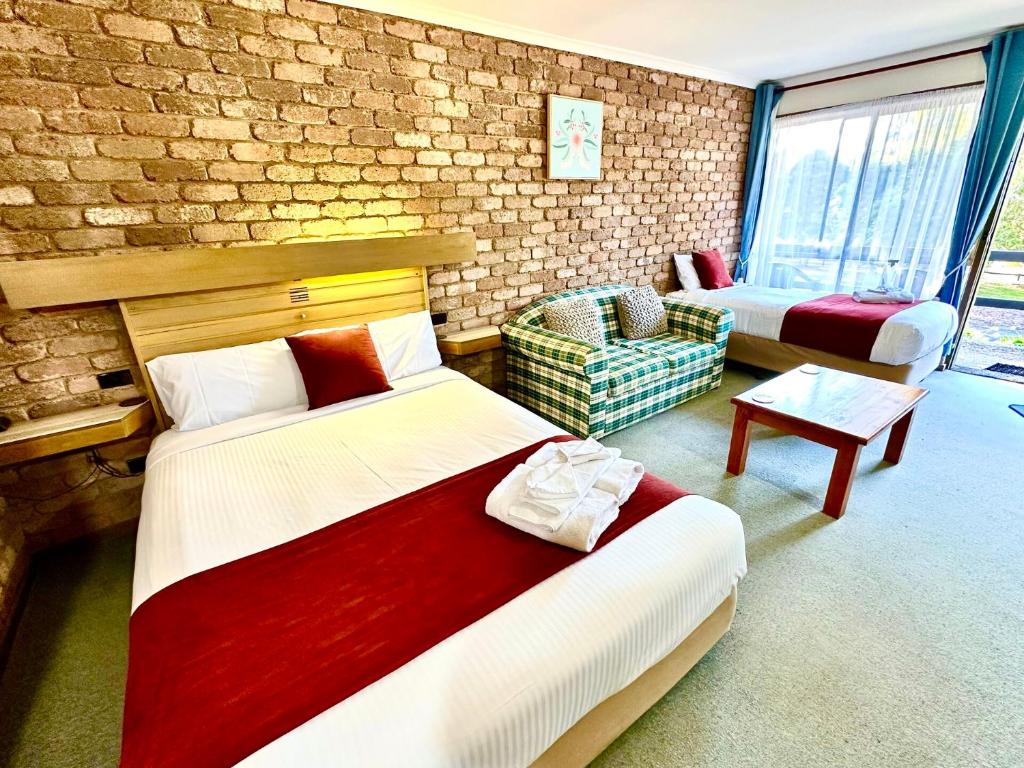 a bedroom with two beds and a chair and a brick wall at Eildon Lake Motel in Eildon