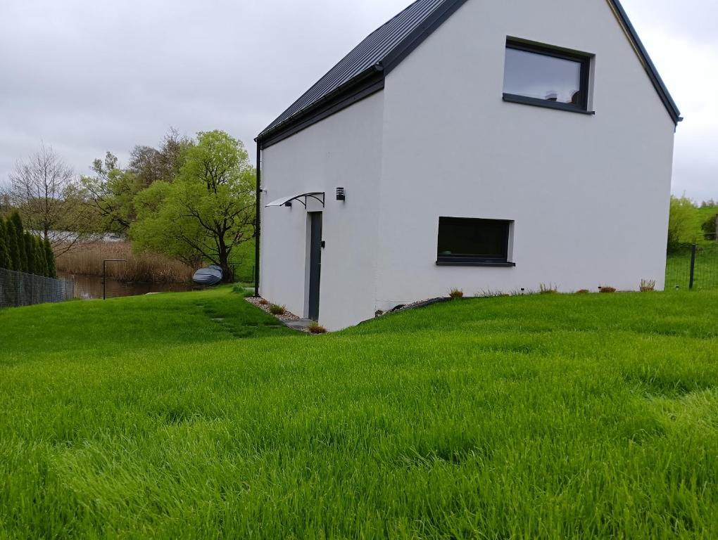 ein weißes Gebäude mit einem Fenster auf einer Wiese in der Unterkunft Domki w Dolinie OSTOJA I, Święta i Sylwester w Nowoczesnych Domkach z Kominkiem nad Jeziorem in Mrągowo