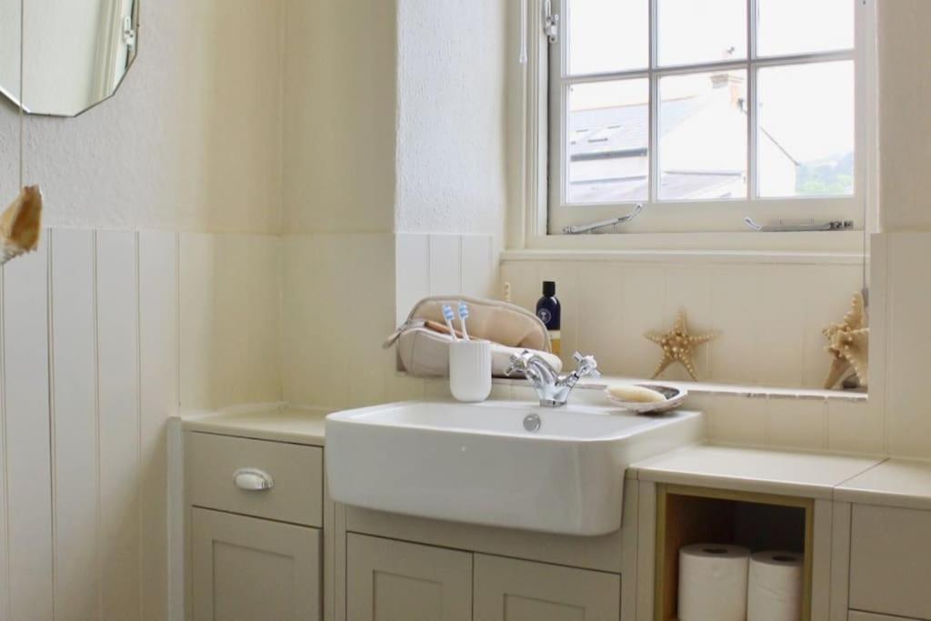 a white bathroom with a sink and a window at Holiday Cottage with Seafront Beach Hut, Lyme Regis, Dorset in Lyme Regis