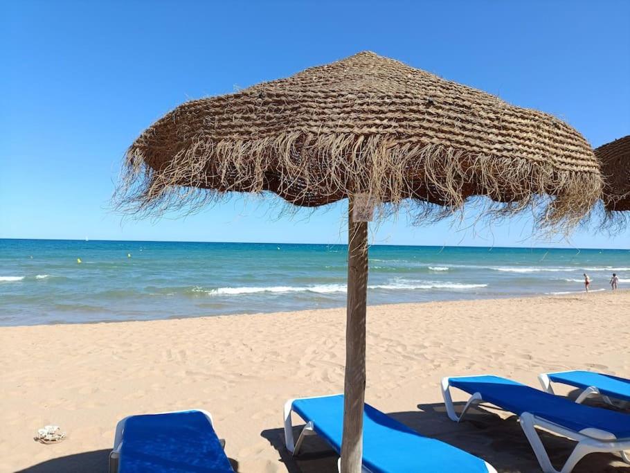 a straw umbrella and chairs on a beach at Sandy Home - Élvezd a tengerpartot! in La Mata
