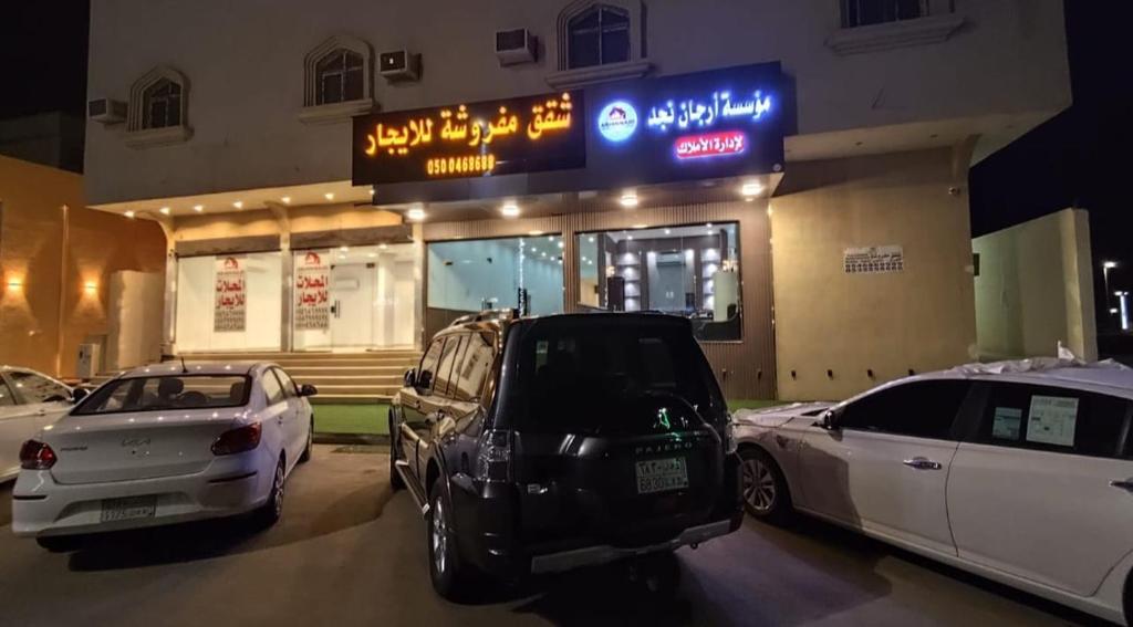 dois carros estacionados num parque de estacionamento em frente a um edifício em شقق ارجان نجد المفروشه em Al Nairyah