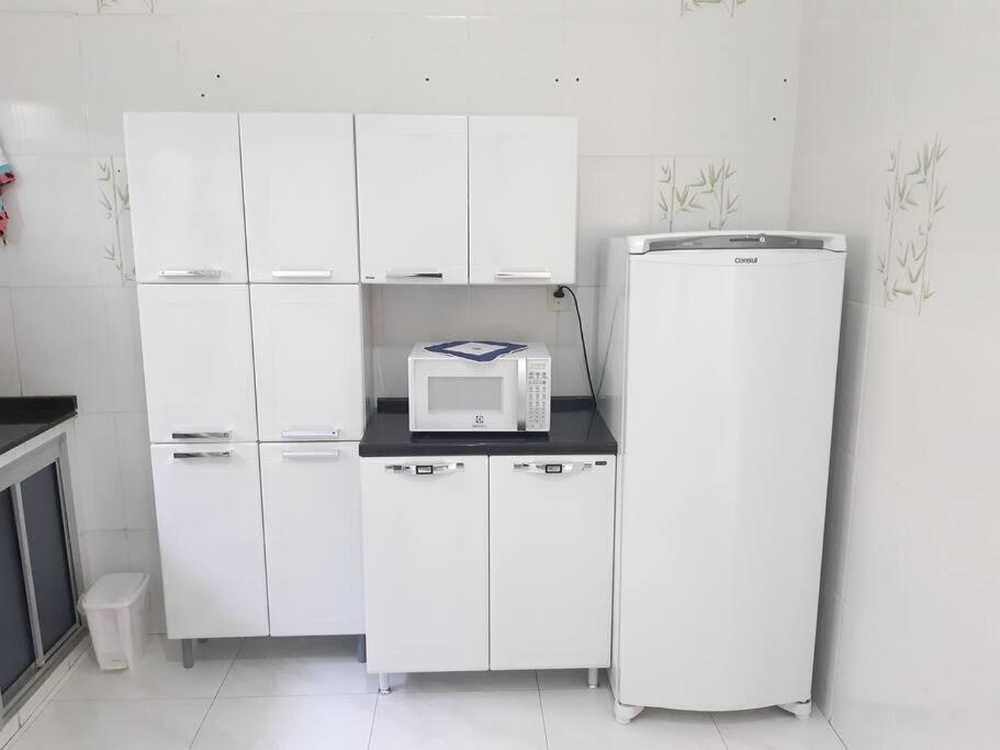 a white kitchen with white cabinets and a microwave on a counter at Casa próximo ao santuário nacional in Aparecida