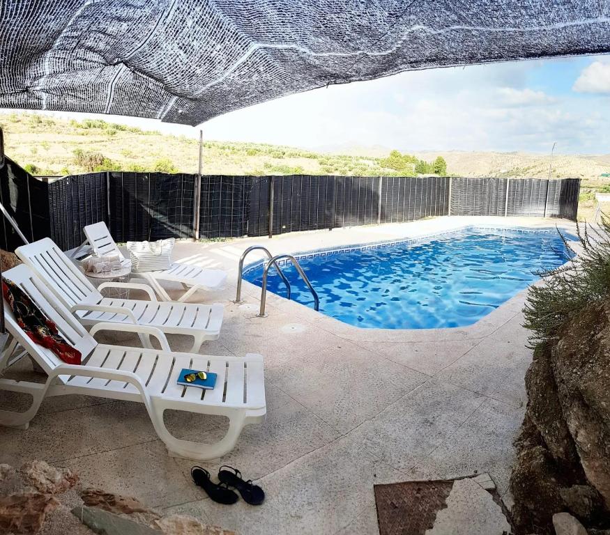 a swimming pool with white chairs and an umbrella at 6 bedrooms villa with private pool enclosed garden and wifi at Velez Rubio in Vélez-Rubio