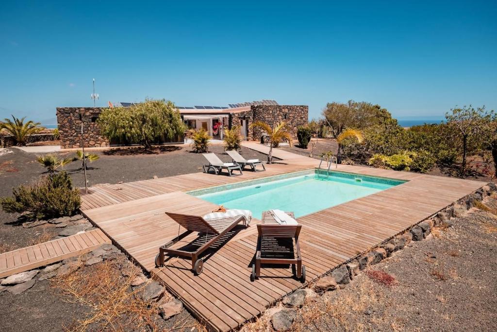 a swimming pool with two chairs and a wooden deck at Ecovilla Haleakala con Piscina y Sauna privadas in Villaverde