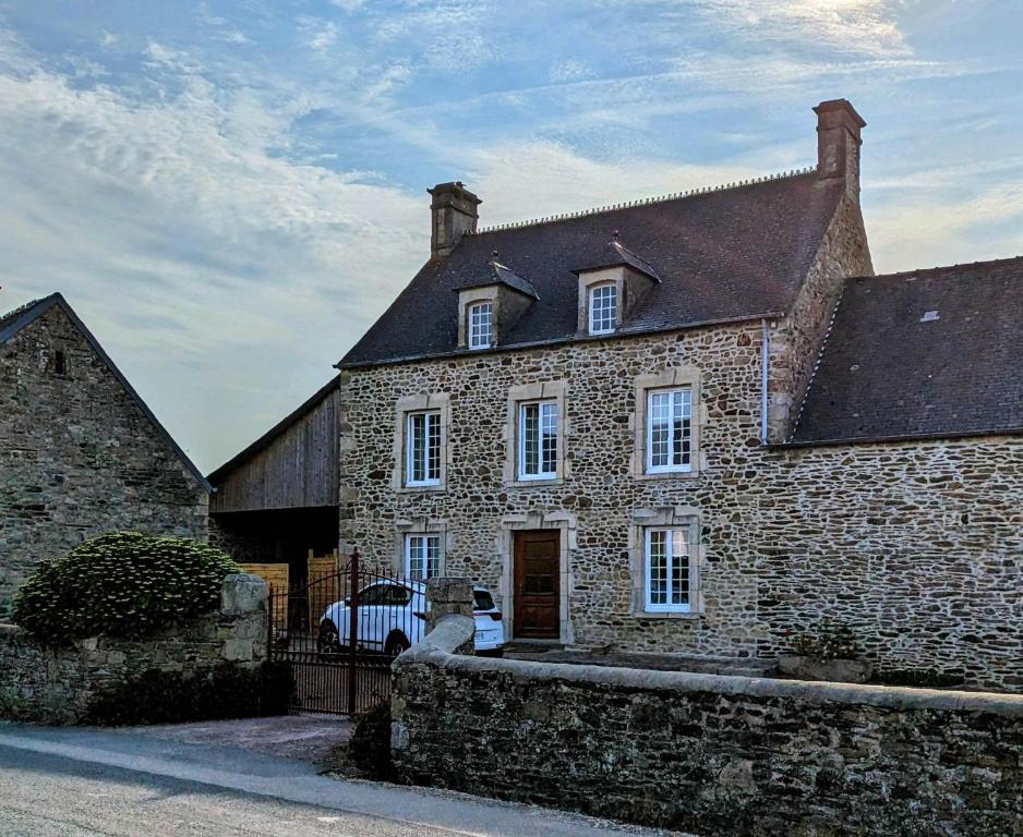 una casa de piedra con un coche aparcado delante de ella en Les Jardins des 3 sœurs, en Quettehou
