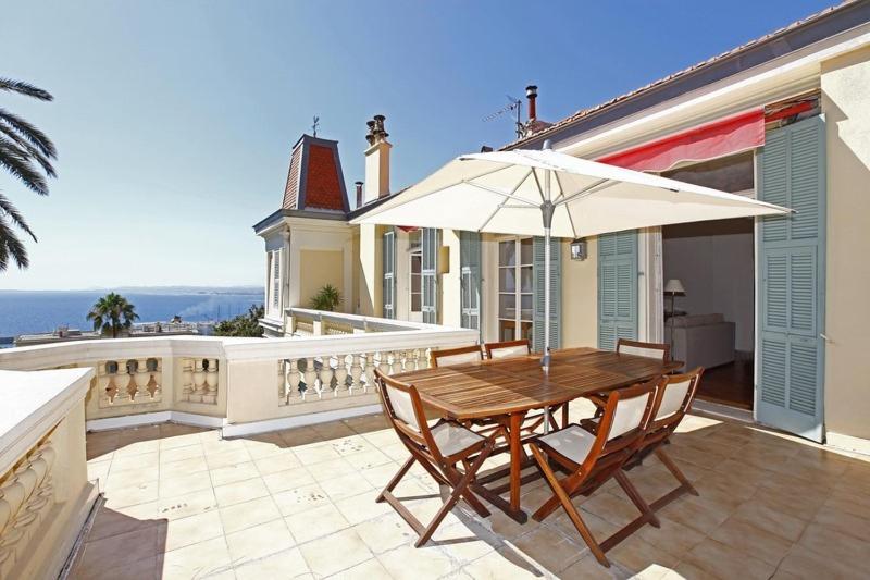 una mesa de madera y sillas con sombrilla en una casa en Magnifique appartement d'époque avec Vue Mer 4 personnes avec terrasse Le Port Nice, en Niza