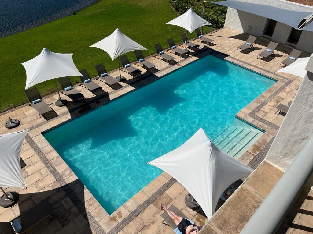 einen Blick über einen Pool mit weißen Sonnenschirmen in der Unterkunft Asara Wine Estate & Hotel in Stellenbosch