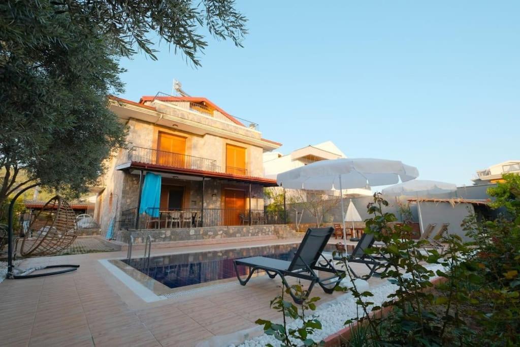 a house with a patio with a chair and an umbrella at Lüks Bahçeli Özel Havuzlu Villa in Fethiye