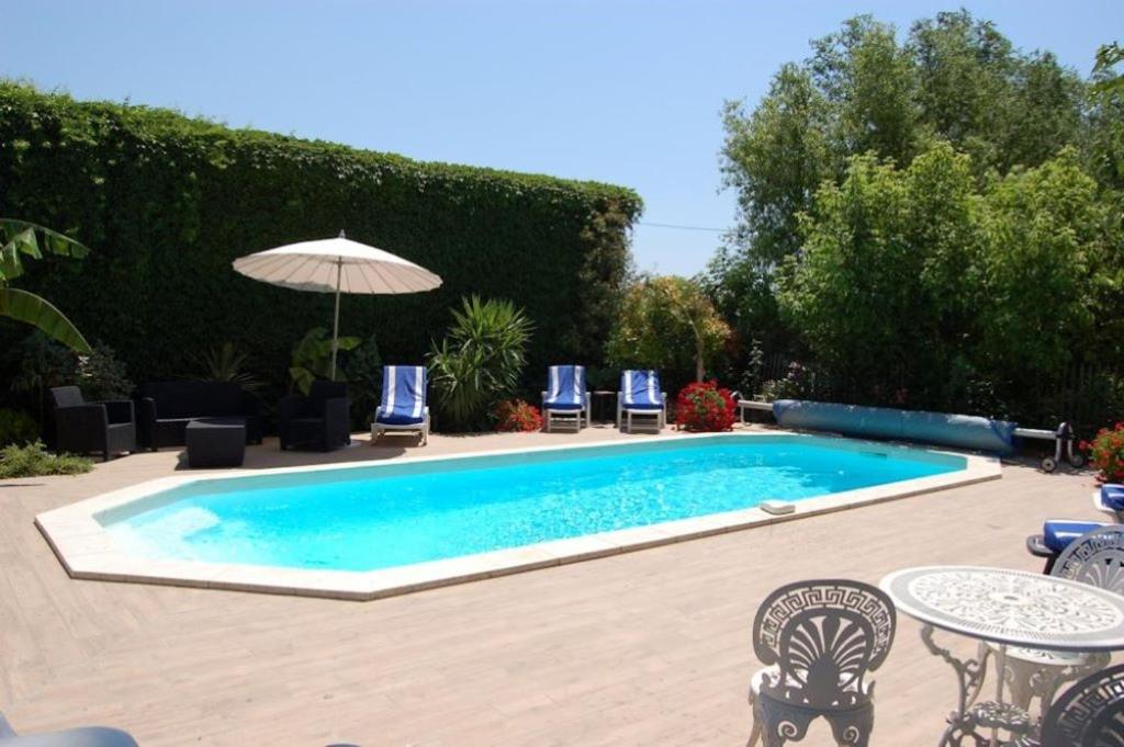 una piscina en un patio con sillas y sombrilla en Chambre BELEM - MAS SAINT LOUIS en Aigues-Mortes