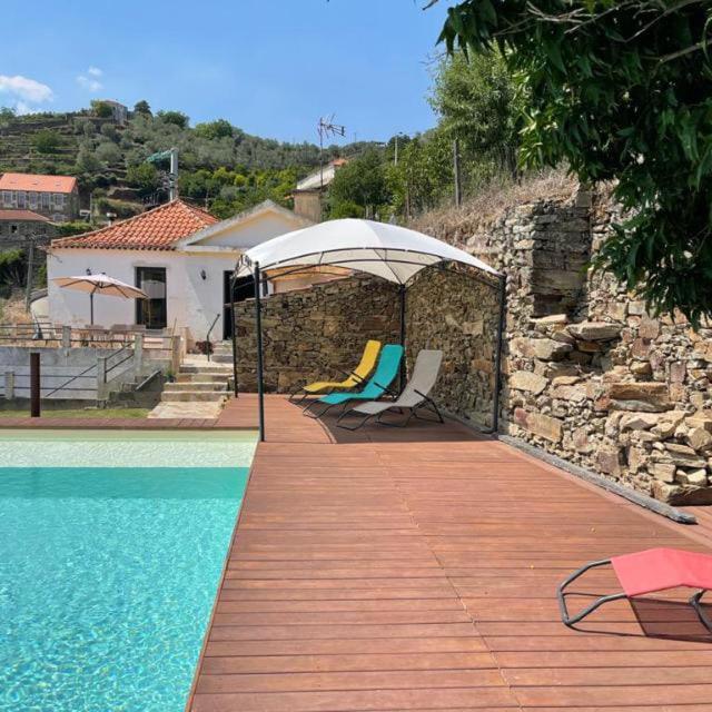 a pool with chairs and an umbrella next to a house at Casa dos Bardos in Alvações do Corgo