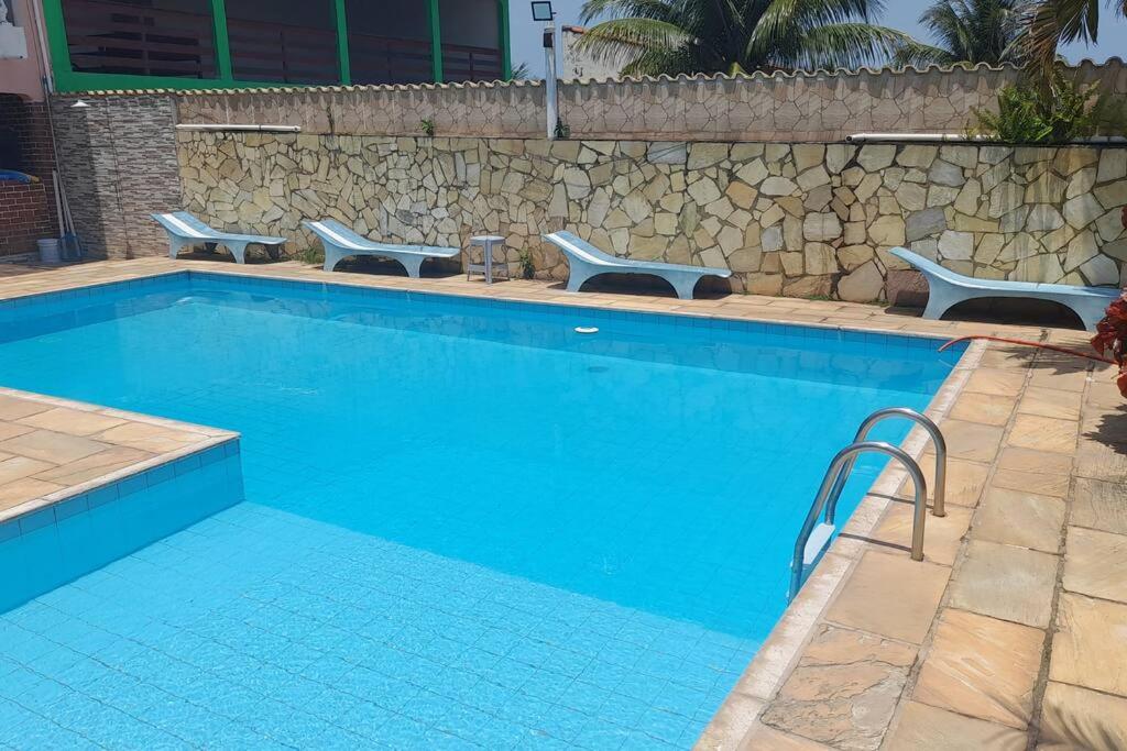 a blue swimming pool with benches and a stone wall at Espaço familiar in Maricá