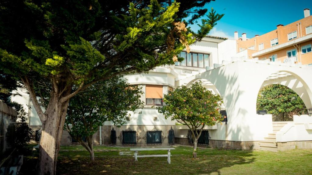 ein weißes Gebäude mit einem Baum und einer Bank in der Unterkunft Espinho Vintage - Alojamento de Charme in Espinho