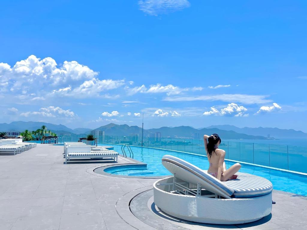 a woman sitting on a chair next to a swimming pool at Panorama Superview Nha Trang Apartment in Nha Trang