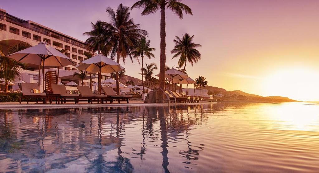 a resort pool with chairs and palm trees and the ocean at Marquis Los Cabos, an All - Inclusive, Adults - Only & No Timeshare Resort in San José del Cabo
