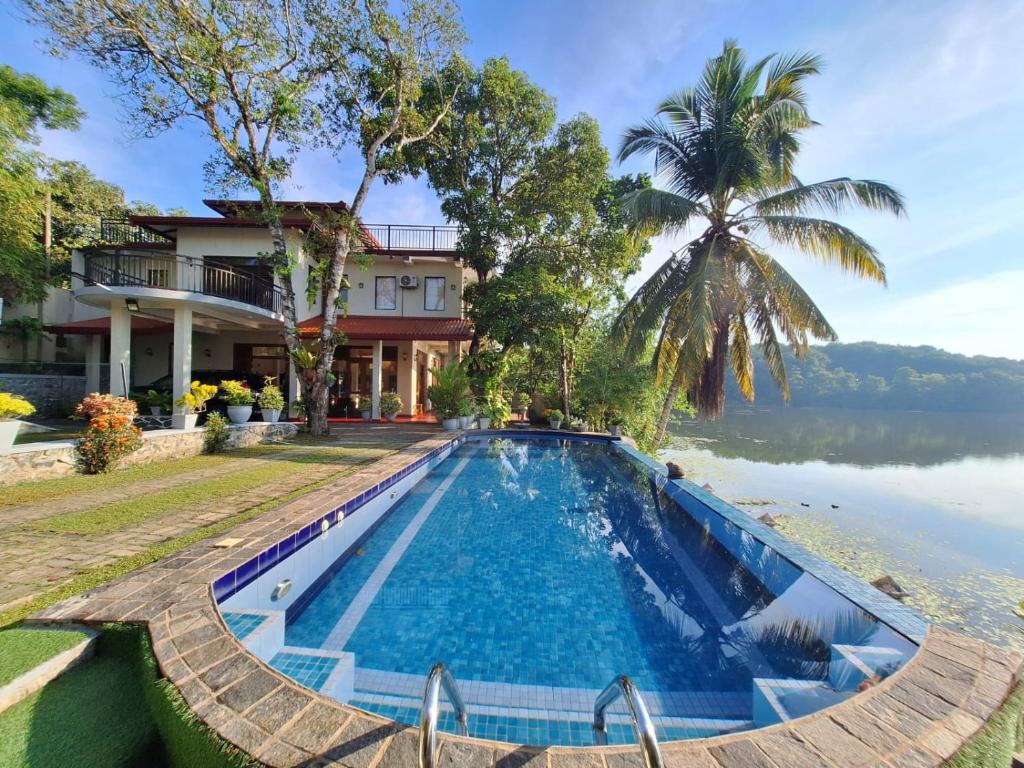 a swimming pool in front of a house next to a lake at MyHoliday Home @ Bandaragama in Bandaragama