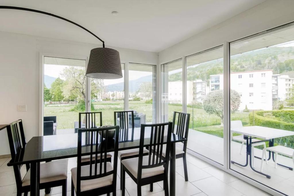 comedor con mesa, sillas y ventanas en Green Caslano Apartment, en Caslano