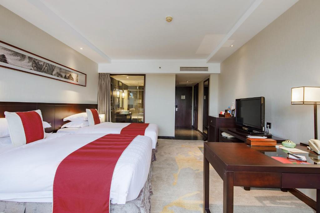een slaapkamer met een bed, een bureau en een televisie bij Garden Hotel Suzhou in Suzhou
