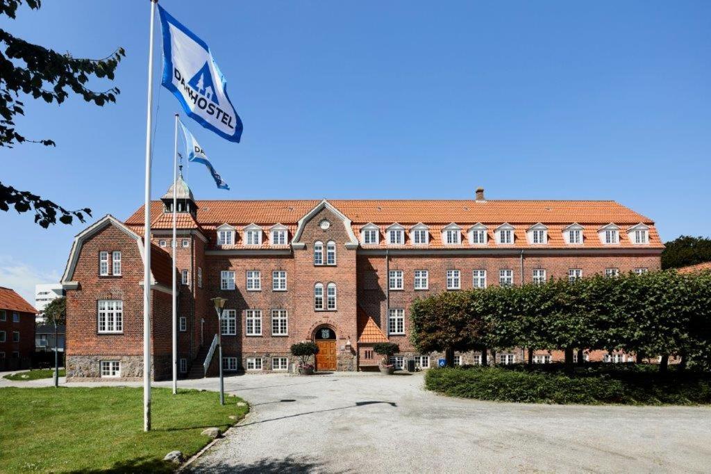 un grand bâtiment en briques avec un drapeau devant lui dans l'établissement Danhostel Esbjerg, à Esbjerg