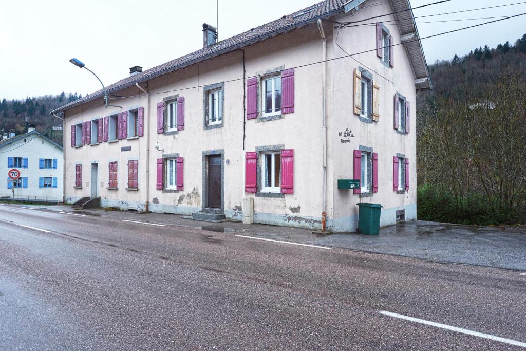 a white building with pink shuttered windows on a street at Le Chtit Appart - Joli appt vue montagne in Cornimont