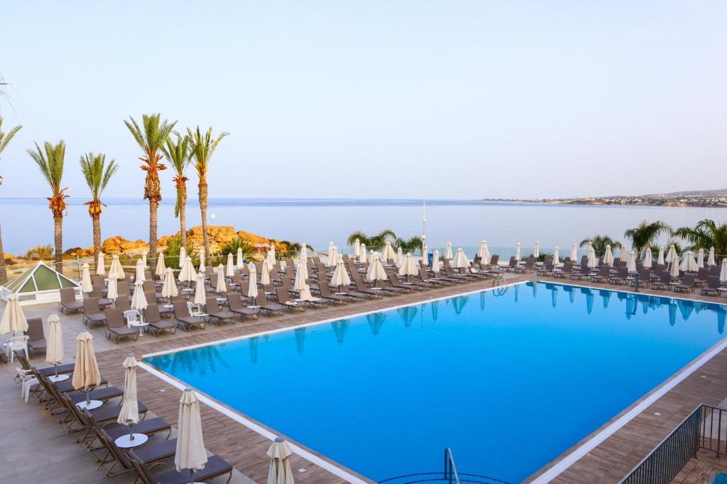 a large swimming pool with chairs and palm trees at Queens Bay Hotel in Paphos