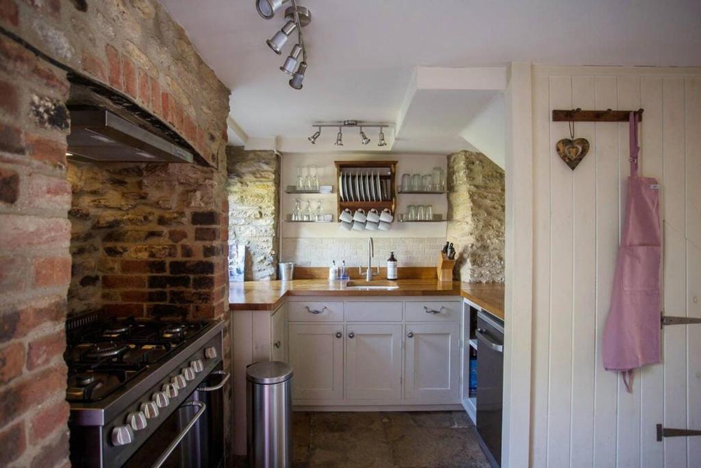 a kitchen with white cabinets and a brick wall at Wishbone Cottage In The Cotswolds in Fairford