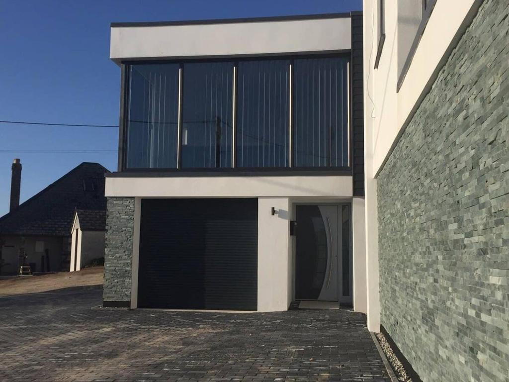 a building with two garage doors next to a brick wall at Relax in style at my stunning Holywell Beach home in Holywell Bay