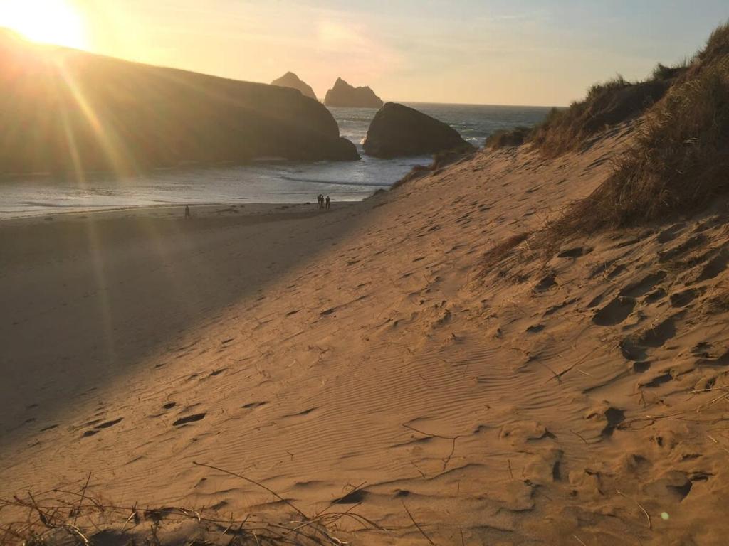 a sandy beach with the sun rising over the ocean at Relax in style at my stunning Holywell Beach home in Holywell Bay