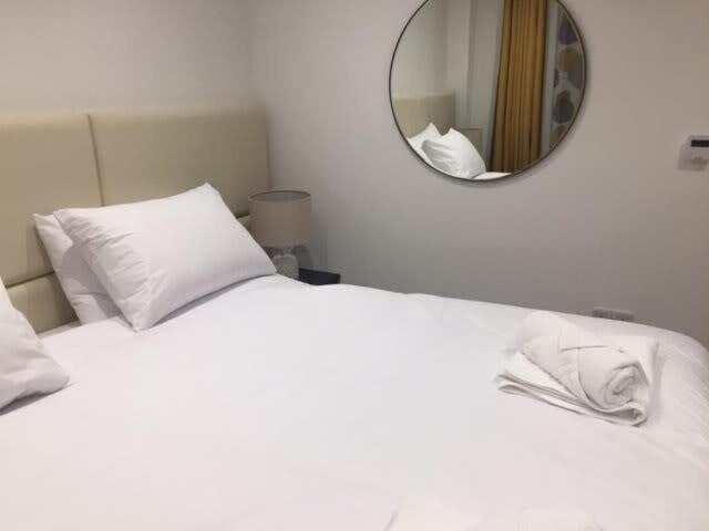 a white bed with a mirror on the wall at Relax in style at my stunning Holywell Beach home in Holywell Bay