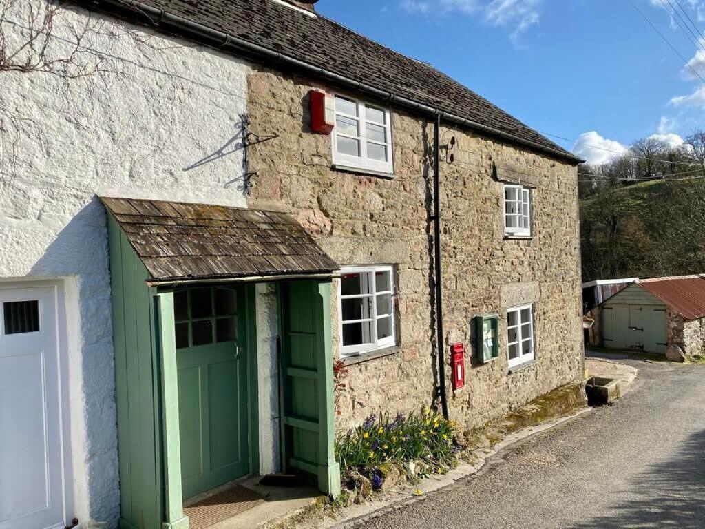 a stone house with a green garage on a street at The Old Post Office A cosy rural gem - Dartmoor in Widecombe in the Moor