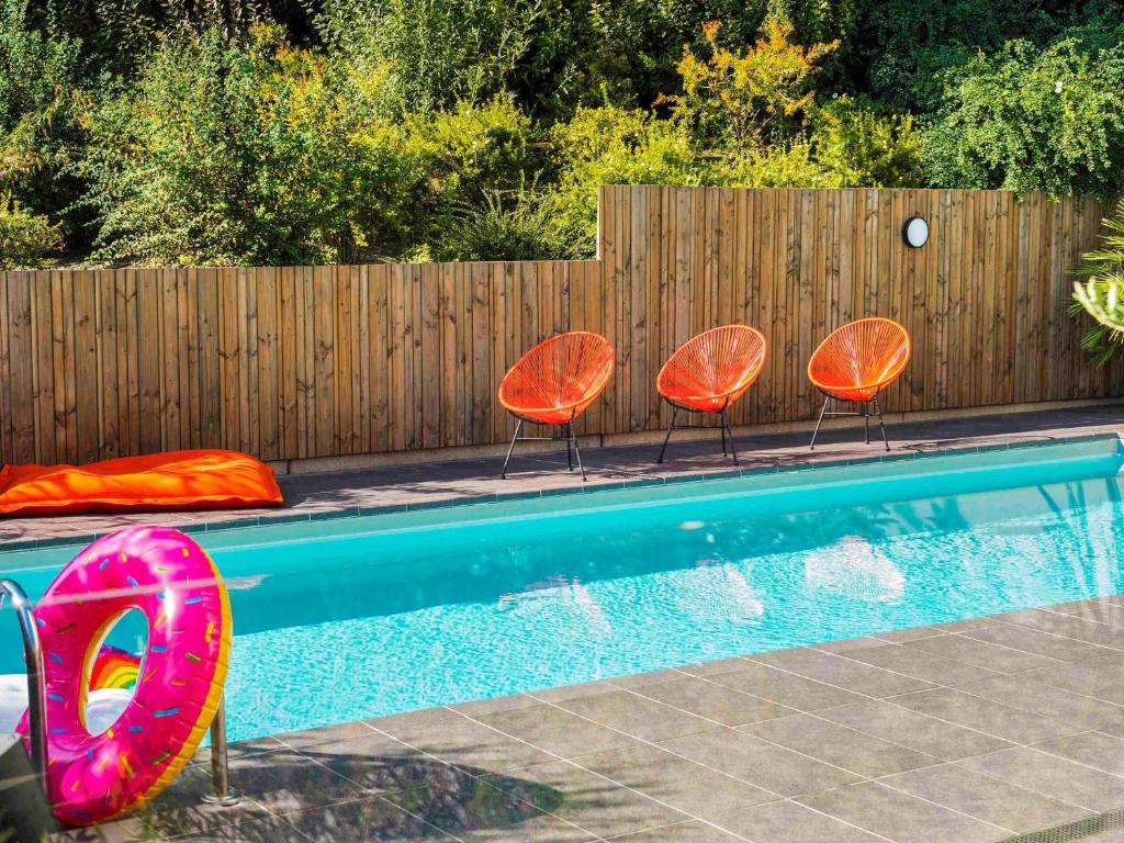 three orange chairs and a swimming pool with a fence at ibis Styles Toulouse Cite Espace in Toulouse