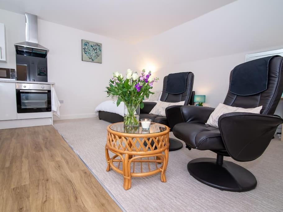 a living room with two chairs and a table with flowers at Studio Apartment ideal for short or long stays in Pershore