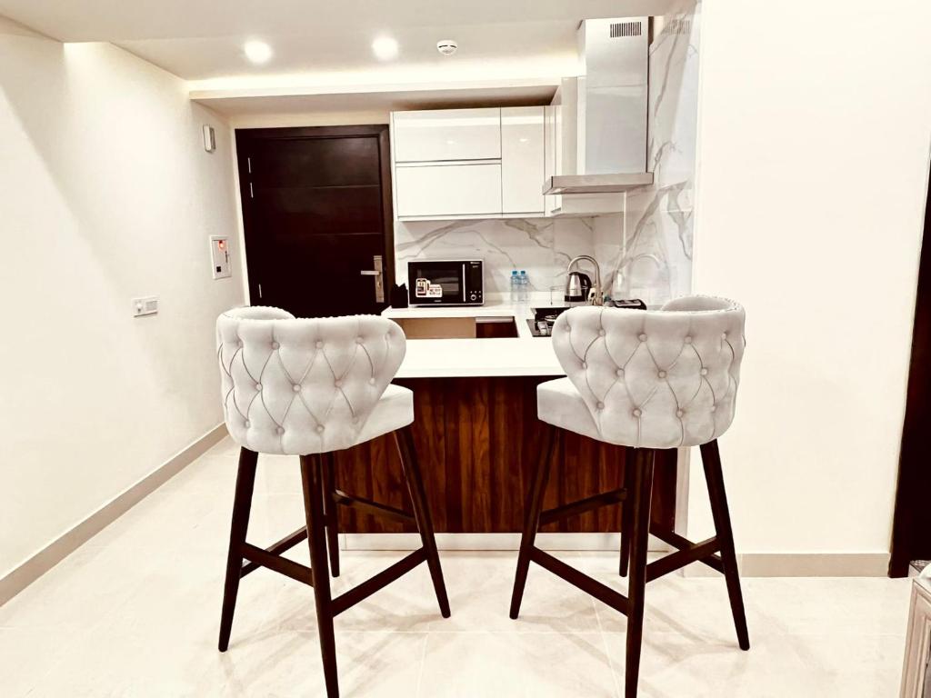 two white bar stools in a kitchen with a counter at Elysium Tower Studio Apartments with Centaurus View, Islamabad by LMY in Islamabad