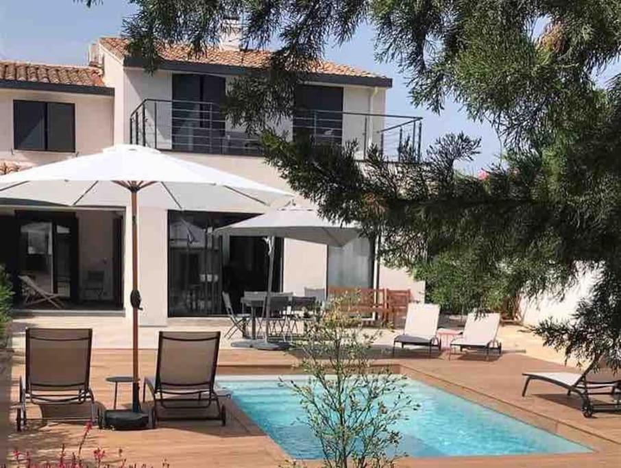 una piscina con sedie e ombrelloni accanto a una casa di Chez Robert - luxueuse villa à proximité des plages avec une piscine privée a La Grande-Motte