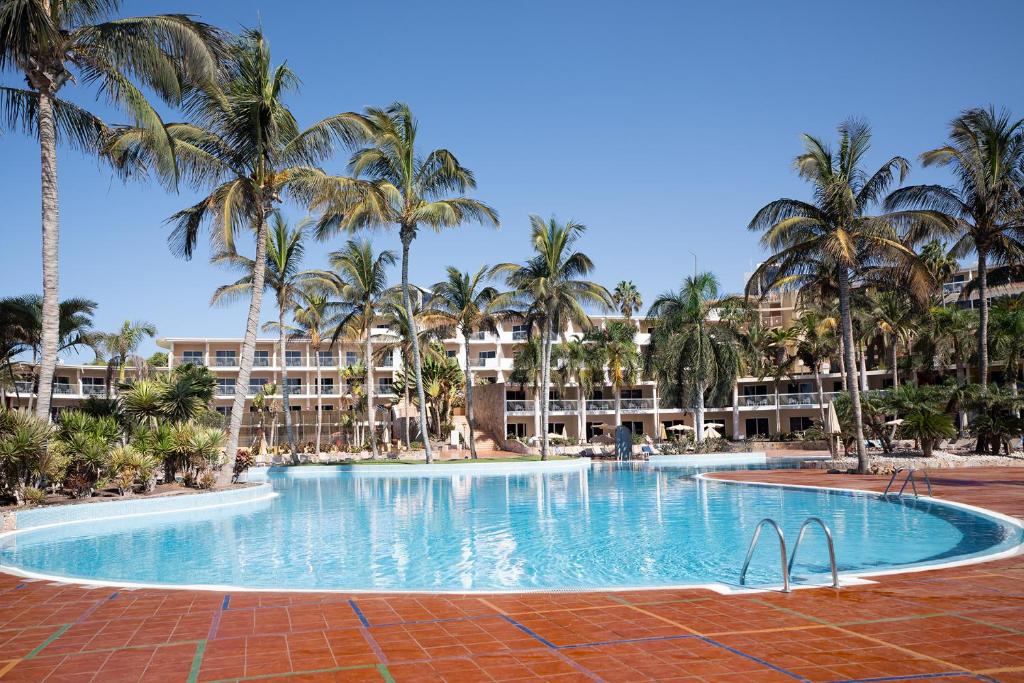a large swimming pool with palm trees in front of a hotel at Club Hotel Drago Park in Costa Calma