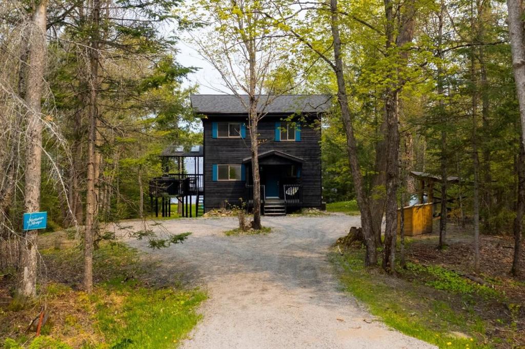 a black cabin in the woods with a driveway at Muskokan Mirage Located on Mirage Lake in Novar