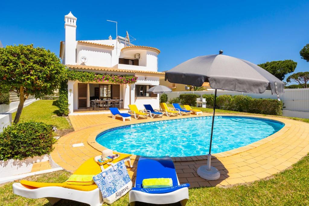 een huis met een zwembad met stoelen en een parasol bij Villa Cavaco in Vilamoura